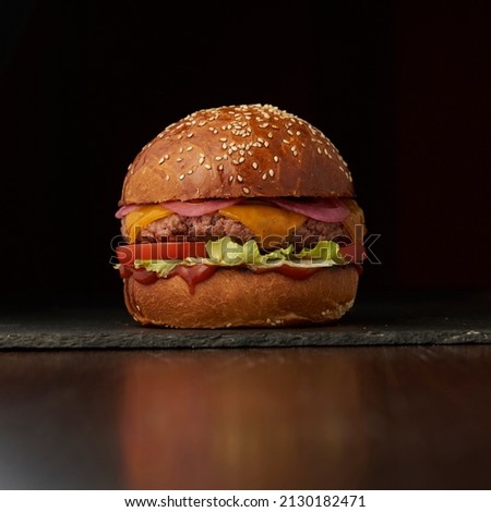 Homemade hamburger close-up with beef, tomato, lettuce, cheese and onion on wooden table. Fast food on dark background 