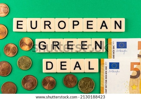 Sentence "European green deal" composed of letters put on the green background with euro cents and 50 euro banknotes.. Photo taken under artificial, soft light