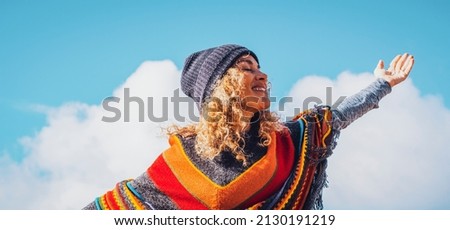 Overjoed adult woman outstretching arms with happy posture. Life balance and happiness for joyful female people smiling and closing eyes against a sunny blue sky. Tourist and travel concept Royalty-Free Stock Photo #2130191219