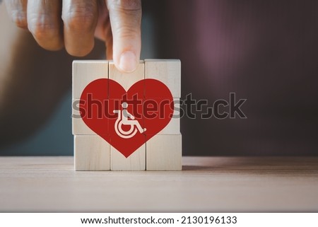 senior 's hand holding wooden cubes with disabled people in red heart symbols,  aged senior nurse care, disabilities health care concept, service business and smart city for aging society
