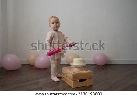Cute baby celebrates birthday with a cake, on a white wall background, a little girl in pink is one year old, lifestyle