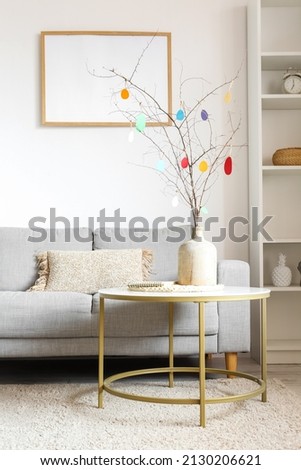 Vase with tree branches and Easter eggs on table in interior of living room