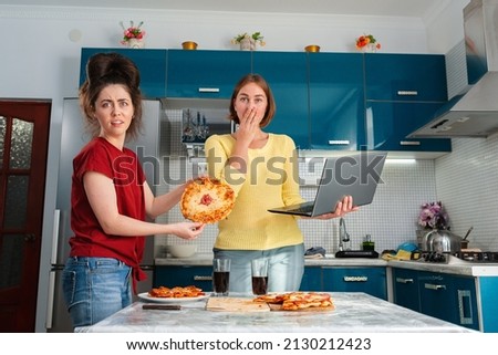 Two young women baked a pizza and were upset with the result, comparing it with pictures of pizza on the Internet. The concept of the Internet, cooking, and LGBT couples.