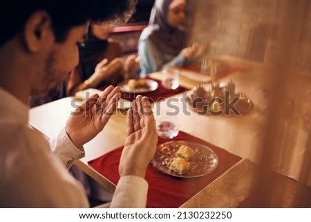 Close-up of Muslim man praying while eating with his family during Ramadan at home.  Royalty-Free Stock Photo #2130232250