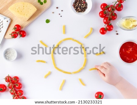 The sun from pasta makes a child's hand on a white table