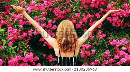 Beautiful happy woman raising her hands up in garden on roses flowers background, back view