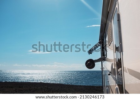 Tourism and summer holiday vacation people excited with arm and hat outside the camper van window admiring ocean freedom feeling. Vanlife and nomadic people lifestyle concept
