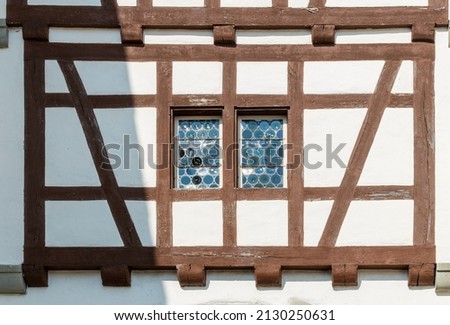 Brown wooden half-timbered wall with white walls and stained glass window in the middle. Beautiful historical piece of wall of building in Swiss old town on sunny summer day Royalty-Free Stock Photo #2130250631