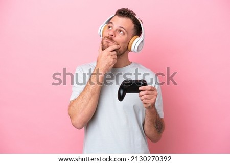 Young Brazilian man playing with video game controller isolated on pink background looking up while smiling
