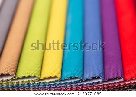 Fabric swatches in different colors are stacked for selection. A variety of shades of upholstery material for furniture and interior. Fabric texture close up. A set of multi-colored rolls of material.