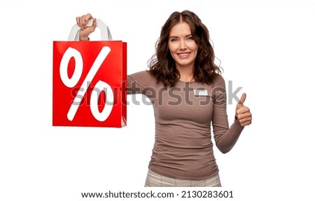 sale and business concept - happy female shop assistant or saleswoman holding shopping bag with percentage sign showing thumbs up over white background