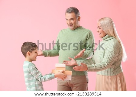 Little boy giving presents to his grandparents in warm sweaters on pink background