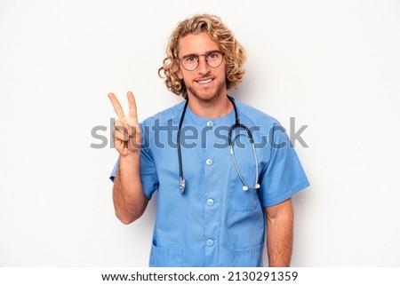 Young nurse caucasian man isolated on white background joyful and carefree showing a peace symbol with fingers.