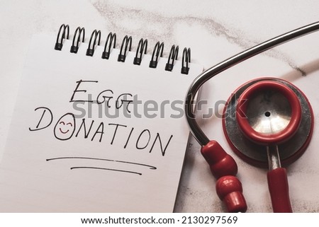 Egg donation handwritten text with smiley face on notepad with stethoscope. In-vitro fertilization, surrogacy concept. Royalty-Free Stock Photo #2130297569