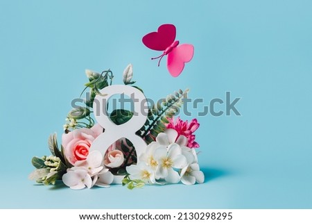 March 8th composition with number and flying butterfly and flowers against pastel blue background. Natural greeting banner for International Women's Day. Creative Mother's day floral concept. Royalty-Free Stock Photo #2130298295