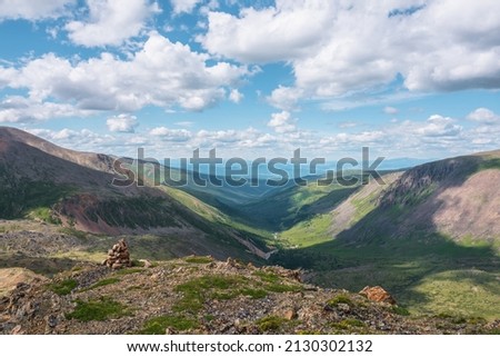 Scenic view from mountain pass to green forest valley among mountain ranges and hills on horizon at changeable weather. Green landscape with sunlit mountain vastness under cumulus clouds in blue sky. Royalty-Free Stock Photo #2130302132