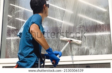 Male professional cleaning service worker in overalls cleans the windows and shop windows of a store with special equipment Royalty-Free Stock Photo #2130306539