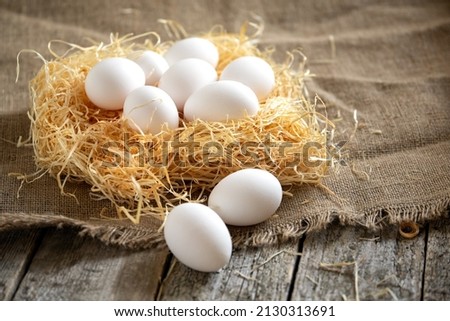 White chicken eggs in straw or hay nest on a burlap sackcloth on rough wooden country table.Still life rustic stile