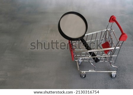Magnifying glass inside shopping trolley. Product search and frugal shopping concept.