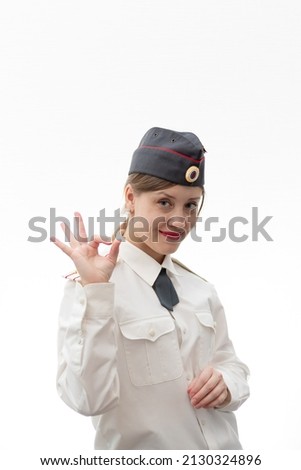 Beautiful young female Russian police officer in dress uniform shows hand signs perfectly and smiles on a white background. Selective focus. Portrait