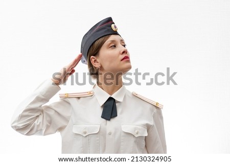 A beautiful young female Russian police officer in dress uniform and a white shirt on a white background salutes the commander. Selective focus. Portrait