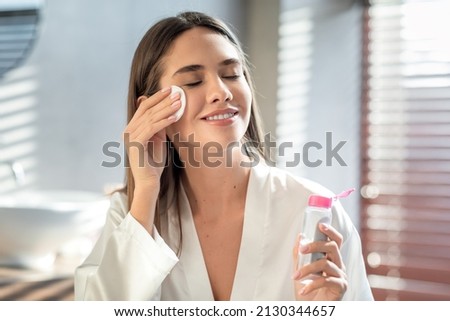 Beautiful Smiling Woman Cleansing Skin With Micellar Water And Cotton Pad While Making Daily Beauty Routine In Bathroom, Attractive Young Female Enjoying Home Skincare Treatments, Copy Space Royalty-Free Stock Photo #2130344657