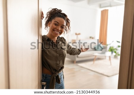 Welcome To My Home. Joyful Millennial Black Lady Opening Door And Gesturing Inviting To Come In Standing Indoors, Smiling To Camera. Real Estate Owner. Hospitality Concept Royalty-Free Stock Photo #2130344936