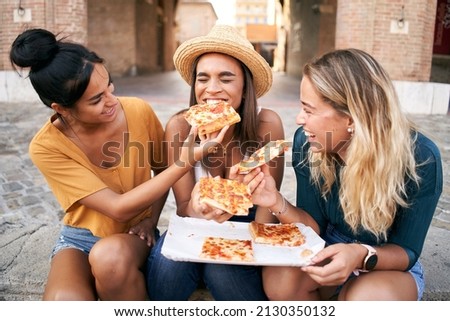 Happy girlfriends eating pizza street food at the city. Female tourist group of three woman having fun. One girl feeds the other. Lifestyle and friendship concept Royalty-Free Stock Photo #2130350132