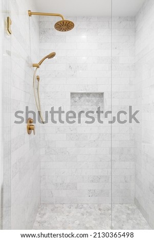 A luxury shower with a gold faucet and shower head, marble subway tile walls, and marble hexagon tile shelf and floor. Royalty-Free Stock Photo #2130365498