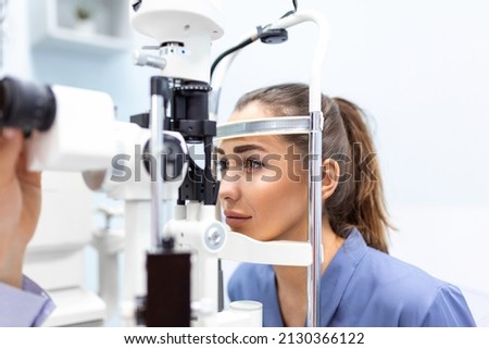 Attentive optometrist examining female patient on slit lamp in ophthalmology clinic. Young beautiful woman is diagnosed with eye pressure on special ophthalmological equipment. Royalty-Free Stock Photo #2130366122