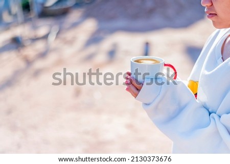 A young woman holds a cup of hot drink in her hand.