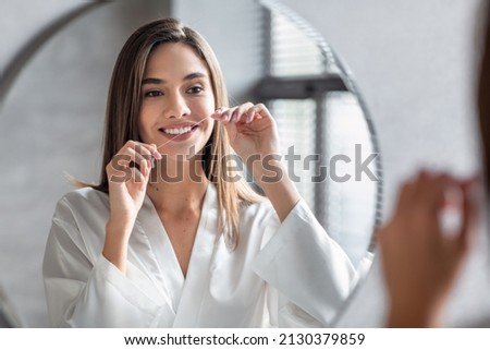 Oral Care. Smiling Young Female Using Dental Floss Near Mirror In Bathroom, Beautiful Millennial Woman Cleansing Teeth, Making Daily Hygiene Routine At Home, Seletive Focus On Reflection Royalty-Free Stock Photo #2130379859