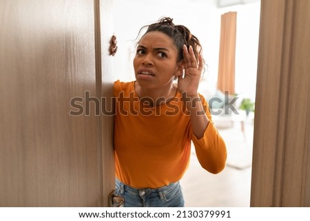 Displeased Black Lady Listening Holding Hand Near Ear Standing In Opened Door Having Problem With Soundproof At Home. Concerned Woman Hearing Something Openind Door Of Her House Royalty-Free Stock Photo #2130379991