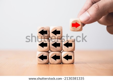 Hand holding red arrow on wooden move on different direction with black arrow on cube for business and technology disruption or unique concept.
