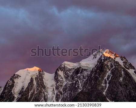 Red fiery cloud in the evening over the silhouette of sharp mountains. Top black rocks in evening golden sunshine and white-snow pointy peak. Magnificent purple sunset in the mountains. 