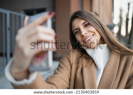 Joyful young woman taking selfie on smartphone in the street