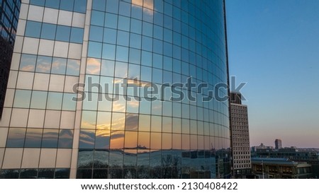 Beautiful tall and rounded glass building with reflective facade shows colorful sky at sunset in Manhattan, NY.