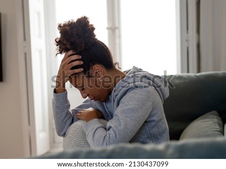 Lonely young African American young woman on sofa feeling pain, exhaustion and sadness. Depressed at home, looking away with sad expressions. In Depression and Mental health concept. Royalty-Free Stock Photo #2130437099