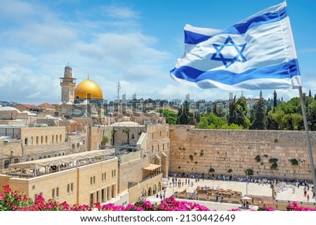 An Israeli flag blows in the wind as jewish orthodox believers read the Torah and pray facing the Western Wall, also known as Wailing Wall in Old City in Jerusalem, Israel.  Royalty-Free Stock Photo #2130442649
