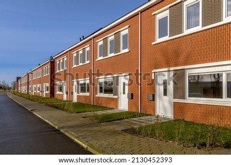 Brand new development of basic public housing in a village in the Netherlands. Neighborhood scene of street with modern suburban terraced houses. Royalty-Free Stock Photo #2130452393