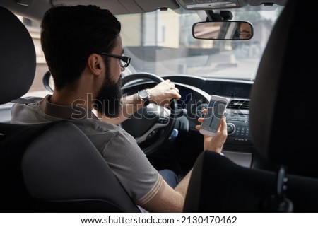 Man searching destination direction or address on gps or navigator application via mobile smartphone inside a car while driving car - back view. Technology, distraction and driving concept