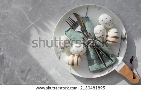 Banner. Table setting. A fashionable marble plate with a rabbit on a napkin, Easter eggs and feathers on a gray background. Top view. Happy Easter holiday concept for cafes and restaurants. Royalty-Free Stock Photo #2130481895