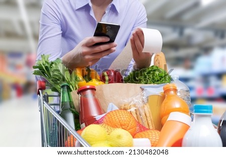 Woman checking the grocery receipt using her smartphone Royalty-Free Stock Photo #2130482048