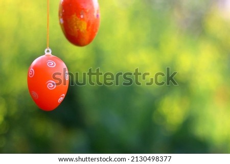 Decorative Easter egg on a tree branch in the garden. Blossom flowers in the background. Selective focus.