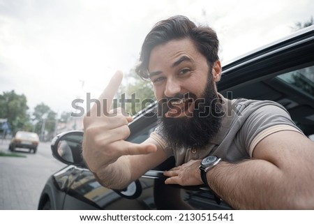 Man, happy to drive his new city car. Cheerful car driver, making funny faces while showing victory or cool sign with hand. A male enjoying driving, happy to travel by car.