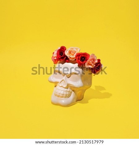 Ceramic skull decorated with colorful flowers, minimal horror layout against bright yellow background. 
