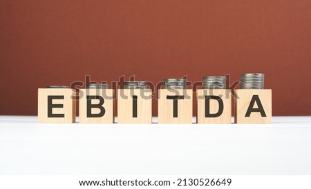 EBITDA text on wooden blocks with coins on brown background, business concept. EBITDA - short for earning before interest taxes depreciation and amortization
