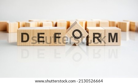 DEFORM - word of wooden blocks with letters on a gray background. Reflection of the caption on the mirrored surface of the table. selective focus