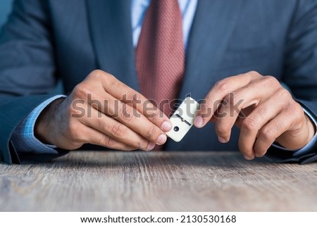 Business man showing domino piece and stacking it by his hand, business strategy background image, wearing blue suit and red tie
