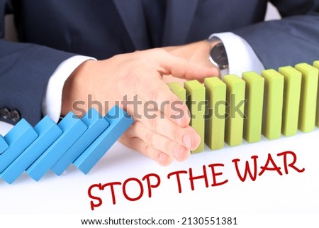 Businessman Stopping The Effect Of Domino With Hand At Desk. Stop War